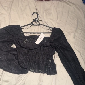 Svart spetsblus från Gina Tricot - Supersnygg svart blus från Gina Tricot i storlek M. Blusen har långa puffärmar och är gjord i ett  spetsmaterial. Smockad midja och fyrkantig urringning .  Ny med prislapp