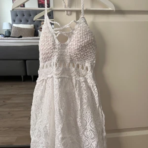 Vit spetsklänning med snörning - Superfin vit kortklänning med spets och virkade detaljer. Klänningen har smala axelband, snörning fram och bak samt en öppen rygg med knyt. Materialet är bomull och spets, vilket ger en romantisk och bohemisk vibe. Perfekt för sommarens alla tillfällen!