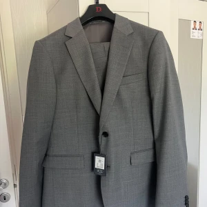 Grå kostym i ullmix från Selected Homme - Säljer en helt ny, oanvänd grå kostym i slim fit-modell. Jacka och byxor i matchande tyg med diskret rutmönster. Perfekt för bröllop, jobbintervjuer eller andra speciella tillfällen. Storlek L normal i passformen, säljes billigt för snabb affär pric kan diskuteras köpt den för 2500kr.