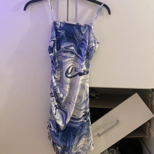 Blåvit mönstrad kortklänning från SHEIN - Säljer en snygg blåvit kortklänning från SHEIN Teen med coolt marmorerat mönster. Klänningen har smala axelband och är figurnära med en lätt rynkad sida. Materialet är mjukt och stretchigt, perfekt för dig som gillar trendiga och unika plagg. Visar även ens former väldigt fint och snyggt.