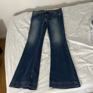 Blå bootcut jeans med vida ben - Säljer ett par blå jeans med riktigt vida ben och bootcut-silhuett. Jeansen har klassisk femficksdesign, snygga slitningar och kontrastsömmar på bakfickorna. Perfekta för dig som gillar retrovibbar och vill sticka ut med en cool look.