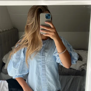 Ljusblå skjorta med puffärmar - Supersöt ljusblå skjorta med puffiga trekvartsärmar och dold knäppning framtill. Klicka gärna på ”köp nu”!