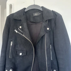Svart skinnjacka från ONLY, stl 36 - Snygg svart skinnjacka från ONLY i storlek 36. Jackan har klassisk bikerstil med silvriga dragkedjor, fickor och detaljer. Materialet är mockaliknande och ger en cool vibe. Perfekt för dig som vill ha en tidlös jacka med edge och stil.