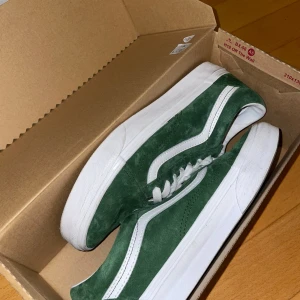 Vans Old Skool gröna sneakers mocka - Snygga Vans Old Skool sneakers i mörkgrön mocka med klassisk vit sidosnöre och vit sula. Skorna har vita snören och en brun yttersula med det ikoniska rutmönstret. Vattenavvisande ytbehandling och stilren design som passar till allt.