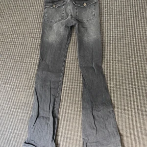 Grå bootcut jeans från RYVLS - Säljer ett par grå jeans från RYVLS i storlek 170. Modellen har bootcut-ben och klassiska fem fickor, med snygga detaljer på bakfickorna. Jeansen har en cool tvättad look och är tillverkade i mjukt jeanstyg. Perfekt för dig som gillar avslappnad stil.
