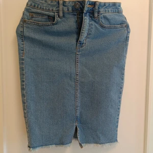 Blå jeanskjol från Noisy May - Säljer en snygg blå jeanskjol från Noisy May i klassisk denim med fransad kant och slits framtill. Kjolen har normal passform, fem fickor och knapp- samt dragkedja i midjan. Perfekt för dig som gillar en chill och trendig stil.