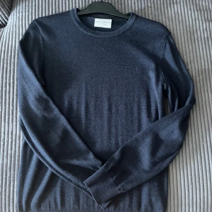 Mörkblå stickad tröja Bruun & Stengade - Snygg mörkblå stickad tröja från Bruun & Stengade. Klassisk rund halsringning och långa ärmar. Tröjan är tunnstickad och passar perfekt till lager-på-lager-stil. Enkel och stilren design med diskret logga på bröstet. Nypris/köpt: 800kr 