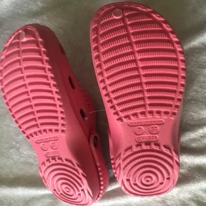 Rosa sandaler  - Säljer ett par rosa sandaler med hålmönster och justerbar hälrem. Skorna är lätta och perfekta för varma dagar eller som inneskor. Sulan är mönstrad för extra grepp och komfort. Stlk 36-37 ,37-38 kvar 