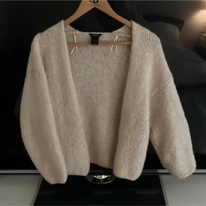 Beige stickad kofta  - Mysig beige stickad kofta med lös passform och långa ärmar. Perfekt att slänga på sig över en topp för extra värme. Enkel och stilren design utan knappar eller dragkedja.