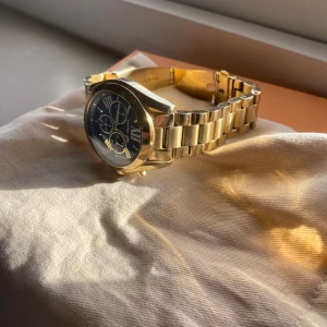 Guldfärgad klocka med blå urtavla - Stilren klocka från Michael Kors i guldfärgat metallarmband och blå urtavla med romerska siffror och flera små urtavlor. Perfekt accessoar för dig som gillar klassisk och lyxig design.