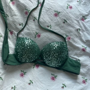 Calzedonia bikini med paljetter  - Säljer en snygg grön bikiniöverdel från Calzedonia med glittriga paljetter på kuporna. Bikinin har halterneck-band och vadderade kupor för extra stöd. Perfekt för dig som vill sticka ut på stranden!