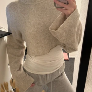 Beige stickad croppad polotröja från Monki - Säljer en beige stickad croppad polotröja från Monki. Tröjan har långa, vida ärmar och en hög polokrage. Perfekt för lager-på-lager och riktigt mysig att bära under kyliga dagar.