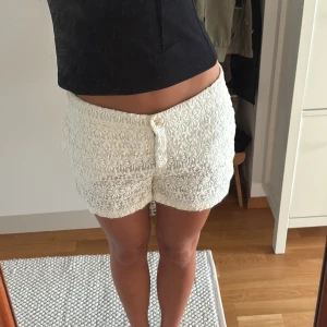 Vita spets shorts från Zara Woman - Säljer ett par vita spets shorts från Zara  med vackert blommigt spetsmönster och dekorativa guldknappar framtill. Shortsen har normal passform.