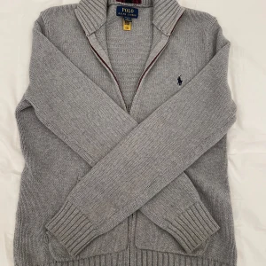 Grå stickad kofta från Polo Ralph Lauren - Säljer en klassisk grå stickad kofta från Polo Ralph Lauren med dragkedja och ribbade muddar. Tröjan har lång ärm och den ikoniska broderade loggan på bröstet. Är storlek L i barn storlek och passar personer som är cirka 155-164! Har inga defekter! 100% äkta✅ Nypris 1595 men säljer för 450! Skriv om ni har några funderingar!