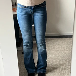 Blå bootcut jeans - Säljer ett par klassiska blå bootcut jeans med normal passform och hög midja. Jeansen har fem fickor, dragkedja och knapp framtill. Perfekta för dig som gillar en tidlös stil med lite utsvängda ben.