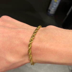 Guldfärgat tvinnat armband - Säljer ett snyggt armband i guldfärg med tvinnad design. Armbandet har en klassisk och stilren look som passar perfekt till dig som gillar accessoarer med lite extra detalj. Perfekt att bära ensam eller kombinera med andra smycken.