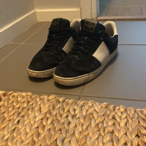 Svarta och vita sneakers från Valentino - Säljer ett par snygga svarta och vita sneakers från Valentino med klassisk design. Skorna har svart ovandel i mocka och vita detaljer i skinn, samt svart snörning och platt sula. Perfekta för dig som gillar stilrena och exklusiva sneakers. Kan pruta vid snabb affär