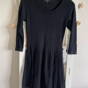 Svart klänning från Lindex - Svart klänning från Lindex med trekvartsärm och rund halsringning. Kjoldelen har en lätt struktur och klänningen har dragkedja i ryggen. Perfekt för dig som gillar enkel och stilren design.