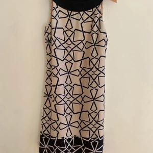 Beige och svart mönstrad klänning från Steinmann, stl 36 - Säljer en snygg beige klänning från Steinmann med svart grafiskt mönster och svarta detaljer vid hals och nederkant. Klänningen är ärmlös och har en rak passform. Fodrad inuti och med fint fall. Helt ny, aldrig använd! 