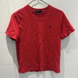 Röd t-shirt från Polo Ralph Lauren - Klassisk röd t-shirt från Polo Ralph Lauren med broderad marinblå logga på bröstet. T-shirten har rund halsringning och korta ärmar. Tillverkad i mjuk  bomull för en skön känsla. Storlek 10-12 år