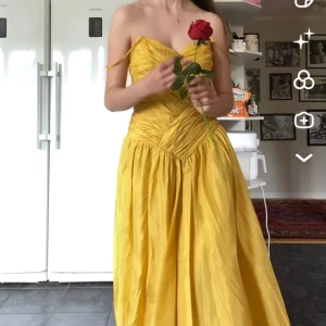 Gul långklänning med draperad överdel - Säljer en solgul långklänning med smala axelband och vackert draperad överdel. Klänningen har markerad midja och ett svepande kjolparti som ger en elegant siluett. Perfekt för bal eller festliga tillfällen. Jag använde denna på spex när jag klädde ut mig till Belle i skönheten och odjuret 