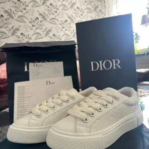 Dior B33 spin sneaker vit  - Säljer ett par stilrena vita sneakers från Dior med diskret mönstrad. Helt nya i storlek 39. Köpa i fel storlek därför säljs de med kvitto och allting. Skorna har snörning och en tjock, platt sula för en modern look. Perfekta för dig som gillar exklusiva och minimalistiska sneakers.