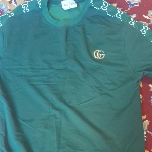 Grön sweatshirt från Gucci med logga - Säljer en grön sweatshirt från Gucci med klassisk GG-logga broderad i guld på bröstet. Tröjan har ribbade muddar och detaljer med GG-mönster längs ärmarna. Perfekt för dig som gillar exklusiva streetwear-plagg. Och en fin äkta gucci keps som man får med i köpet har inte haft 1 månad har änvänt 8 gånger priset kan diskuteras 