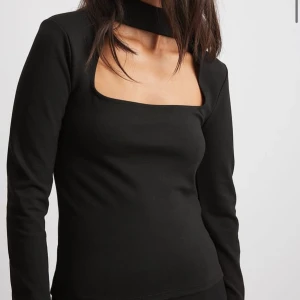 Svart långärmad topp med fyrkantig urringning - Trendig svart långärmad topp med unik fyrkantig urringning och bred halsdetalj. Toppens design ger en modern och stilren look, perfekt att matcha med både jeans och kjol.