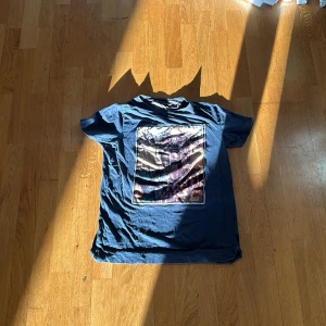 Mörkblå t-shirt med tryck från LIMITATO  - Säljer en mörkblå t-shirt från LIMITATO med ett stort rektangulärt tryck på framsidan. T-shirten har rund hals och korta ärmar. Perfekt för dig som gillar unika prints och en avslappnad stil.