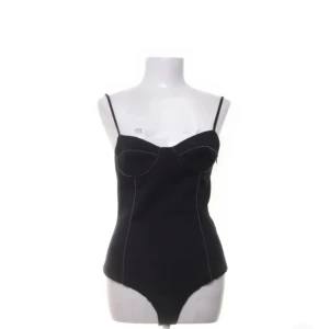 Svart body med tunna axelband från Zara - Säljer en svart body från Zara med tunna axelband och markerade kupor. Bodyn har en stilren design med synliga sömmar och är perfekt för att styla till olika outfits.