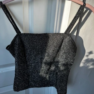 Glittrig svart croppad linnetopp från Gina Tricot - Säljer en glittrig svart croppad linnetopp från Gina Tricot. Toppen har smala axelband och är perfekt för att sticka ut med sin glittriga finish. Snygg att styla till fest eller när du vill glänsa lite extra!