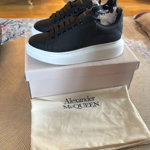 Svarta sneakers från Alexander McQueen - Säljer ett par svarta Alexander McQueen sneakers med vit, chunky plattformssula. Skorna har svart ovandel i skinn, svarta skosnören och guldfärgad logga på häl och plös. Kommer med originalpåse och låda.