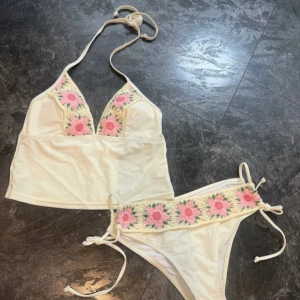 Ljus gul tankini  med virkade blommor - EJ ANVÄND ‼️‼️säljer dessa för dom är för stora på mig. Superfin vit bikini med virkade detaljer i rosa och grönt på både överdel och underdel. Överdelen har halterneck och längre linneform, medan underdelen har knyt i sidorna och bred virkad kant. Perfekt för stranden och för sommaren om man inte vill visa för mycket skinn. 