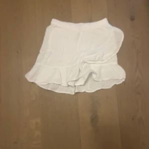 Vit volangkjol från Gina Tricot - Säljer en söt vit kjol från Gina Tricot med volangdetaljer. Kjolen har resår i midjan och är tillverkad i ett lätt och luftigt material, perfekt för varma dagar. Enkel att matcha med olika toppar för en fräsch look. Den är knappt använd 