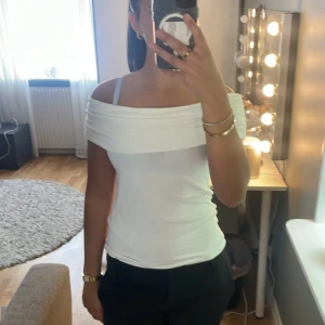 Vit offshoulder topp - Säljer en stilren vit offshoulder topp med bred krage som vilar över axlarna. Toppen är figurnära och har en modern, enkel design som passar perfekt till både jeans och kjol.