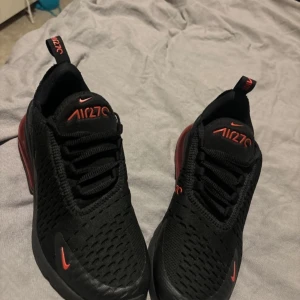 Svarta Nike Air Max 270 sneakers - Säljer ett par svarta Nike Air Max 270 sneakers med röda detaljer och logga. Skorna har en luftig mesh-ovandel, snörning och en tydlig röd Air Max. Som nya använda 2 gånger 