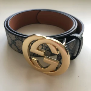 Bälte från välkänt märke - Snyggt bälte med stort guldfärgat G-spänne. Bältet har blått och beige mönster med klassiska G-loggor och insida i brunt skinn. Perfekt accessoar för att lyfta din outfit.