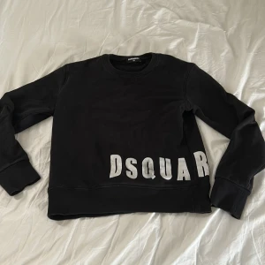 Dsquared2 - Cool svart sweatshirt från Dsquared2 med stor vit DSQUAR-logga tryckt snett över nederdelen. Tröjan har rund halsringning, långa ärmar och ribbade muddar. Perfekt för en avslappnad och trendig stil.