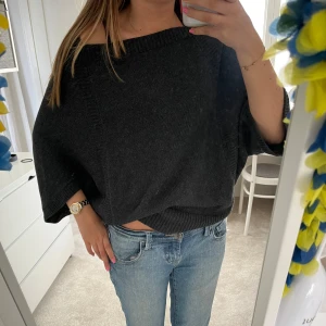 Svart croppad stickad tröja - Svart stickad tröja med bred halsringning som kan bäras offshoulder. Modellen är croppad och har långa, vida ärmar. Perfekt för en avslappnad och trendig look.