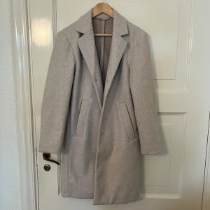 Beige kappa med knappar - Stilren beige kappa med klassisk krage och tre knappar framtill. Jackan har två snedställda fickor och är helfodrad. Perfekt för dig som vill ha en tidlös och enkel look.
