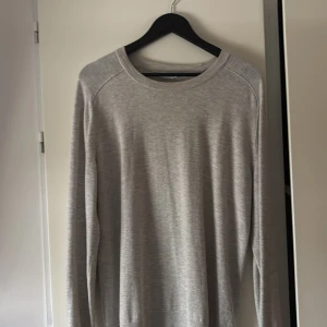 Ljusgrå långärmad tröja Filippa K - En stilren ljusgrå långärmad tröja från Filippa K. Tröjan har en klassisk rund halsringning och är tillverkad i mjukt material som känns skönt mot huden. Perfekt för lager-på-lager och enkel att matcha med olika outfits.