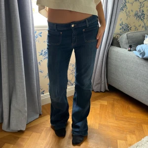 Mörkblå bootcut jeans med låg midja - Snygga mörkblå jeans med bootcut passform och låg midja. Klassisk femficksmodell med kontrastsömmar och mjukt denimtyg. Perfekta för en avslappnad och trendig look.