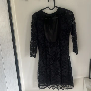 Svart spetsklänning med öppen rygg - Säljer en svart kortklänning i spets med trekvartsärm och öppen rygg. Klänningen har en figurnära passform och fina spetsdetaljer över hela plagget. Perfekt för dig som gillar en elegant och stilren look.