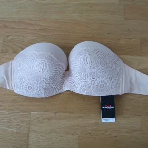  Axelbandslös bh från Wonderbra - Säljer en axelbandslös bh (push-up) från Wonderbra med spetsdetalj över kuporna. Perfekt under toppar och klänningar där du vill ha axlarna fria. Aldrig använd, prislappen sitter kvar.