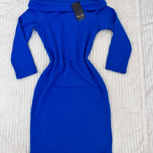 Kornblå offshoulder klänning - Säljer en kornblå, tight klänning med offshoulder-design och trekvartsärm. Klänningen har en figurnära passform och är tillverkad i ett stretchigt material som sitter snyggt på kroppen. Perfekt för dig som vill sticka ut med färg!