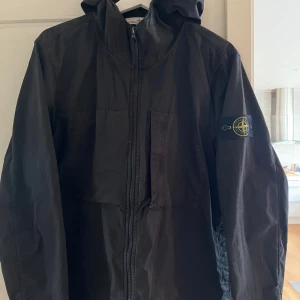 Stone Island jacka - Säljer en svart jacka från Stone Island i bomullstwill med stretch. Jackan har huva, dragkedja framtill och klassisk logotyp på ärmen. Perfekt för dig som gillar stilrena och funktionella plagg.