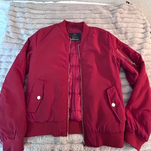 Röd bomberjacka från ONLY, stl S - Snygg röd bomberjacka från ONLY i storlek S. Jackan har klassisk bomberstil med ribbade muddar, dragkedja framtill och fickor med tryckknappar. Materialet är slätt och jackan har en ärmficka med dragkedja för extra edge. Jackan är nästan i nyskick och original priset är 599kr.