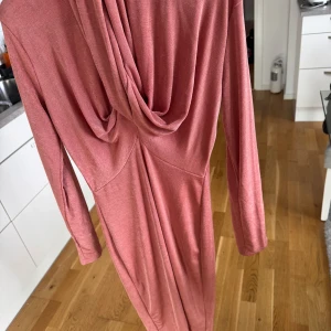 Långärmad rosa klänning med drapering - Säljer en långärmad, rosa långklänning med snygg drapering i ryggen. Klänningen har en mjuk och följsam känsla, perfekt för dig som gillar en stilren men ändå unik look. Passformen är normal och materialet känns lätt och bekvämt mot huden.