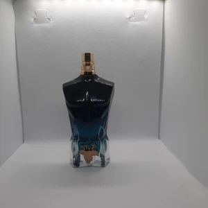 Jean Paul Gaultier Le Male Parfym - Ikonisk herrparfym i en flaska formad som en manlig torso. Flaskan har en snygg blåsvart gradient och detaljer i guld. Glasflaskan är robust och har en lyxig känsla, perfekt som statement på hyllan. Doften är känd för sin fräscha och sensuella karaktär.