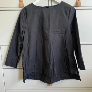 Svart blus från Wera - Säljer en stilren svart blus från Wera i bomull. Blusen har trekvartsärm och en rak, något lös passform. Den har en dold knappslå baktill och slitsar i sidorna. Upplevs gråare på bilderna men är helt svart, inga fläckar eller annat slitage. Passar XS-S.